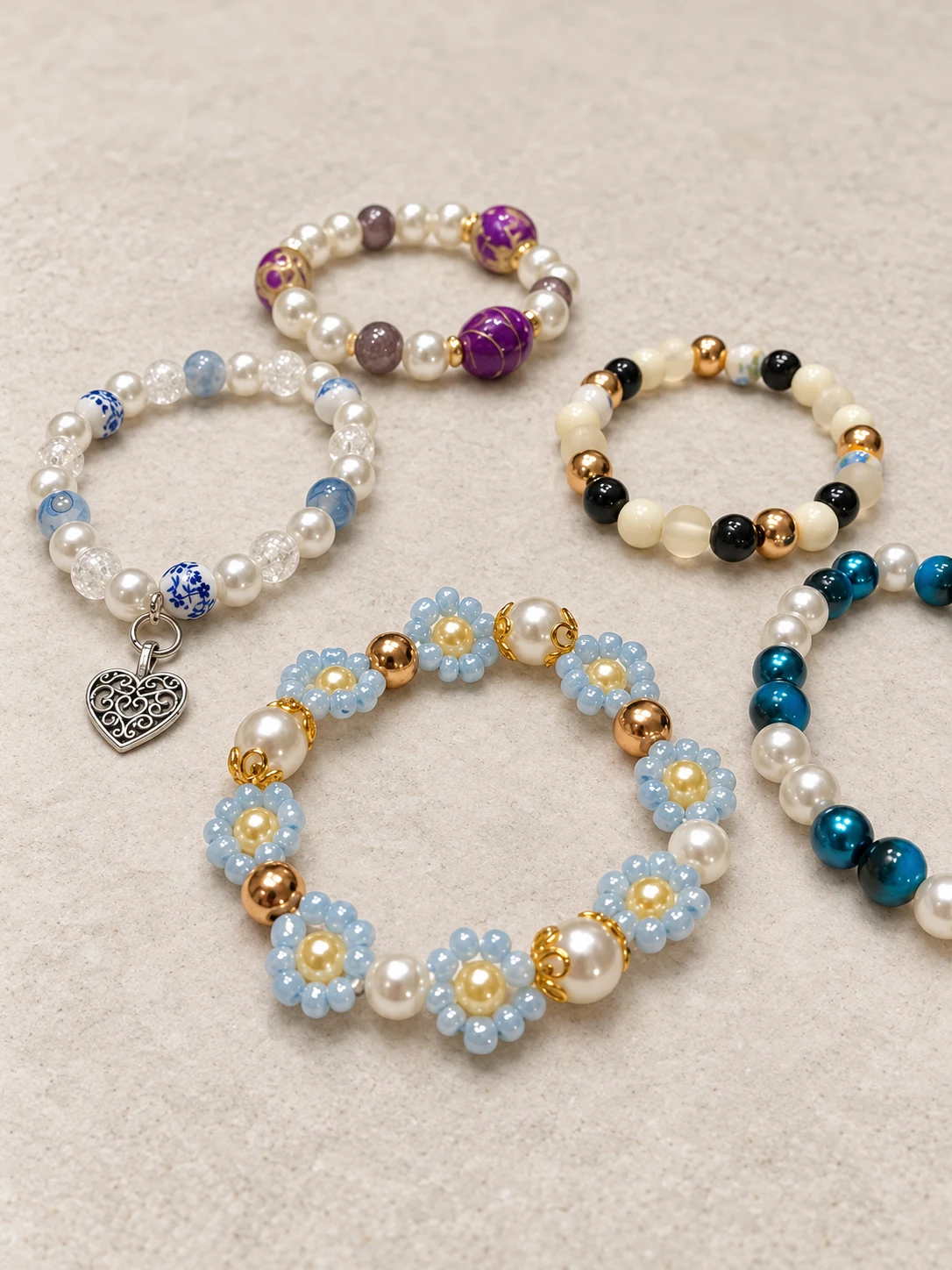 Et utvalg håndlagde armbånd med blå blomster, perler og hjerteanheng